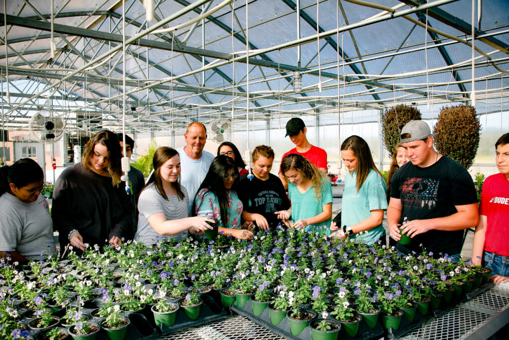 Students engaged in a greenhouse learning activity, creating authentic visual content for community organization and educational marketing campaigns.